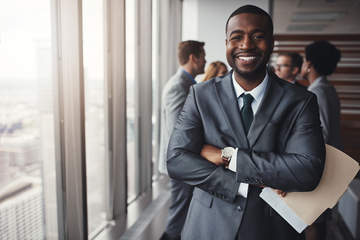 Man smiles at the camera at a career fair holding resume documents.