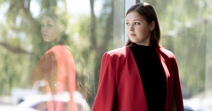 Woman in red coat dramatically looking out window