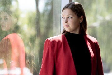 Woman in red coat dramatically looking out window