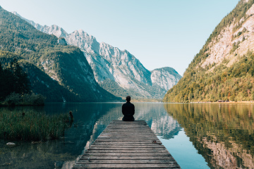 Man meditating by a lake and mountains