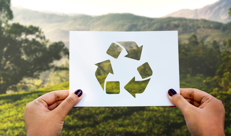 Person holding up recycle sign in front of green landscape