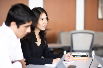 female student in class smiling holding pen 